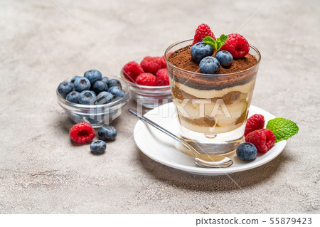 Classic tiramisu dessert with blueberries and raspberries in a glass and bowls with berries on Classic tiramisu dessert with blueberries and raspberries in a glass and bowls with berries on 55879423