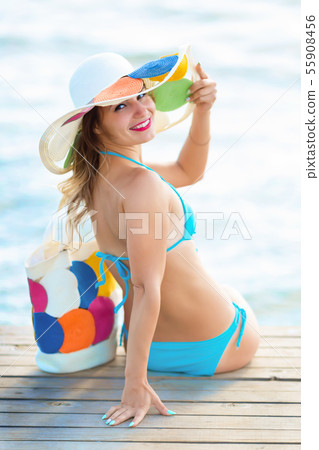 A woman in a swimsuit is sitting on a wooden bridg 55908456