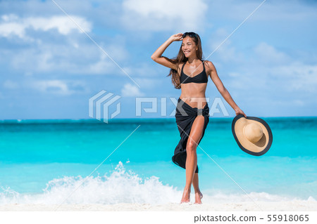 Woman in black bikini and sarong walking on beach Woman in black bikini and sarong walking on beach 55918065