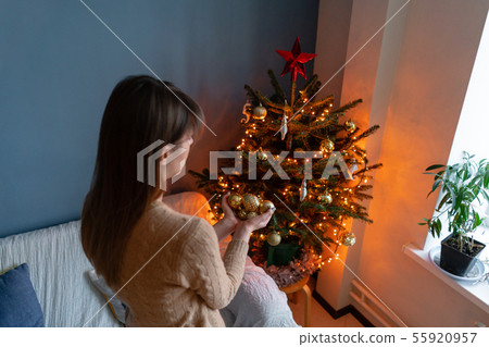 Happy young woman decorating christmas tree at home. Winter holidays in a house interior. Golden and Happy young woman decorating christmas tree at home. Winter holidays in a house interior. Golden and 55920957