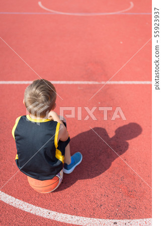 Sad elementary school boy sitting on basketball at Sad elementary school boy sitting on basketball at 55923937