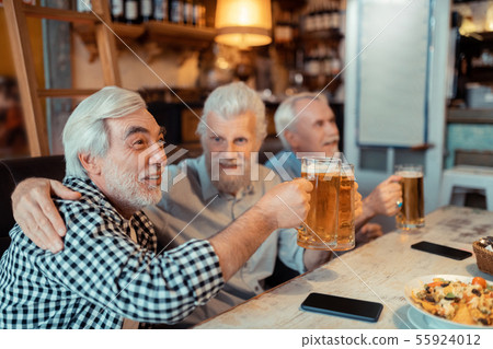 Retired man hugging friend while watching football together Retired man hugging friend while watching football together 55924012