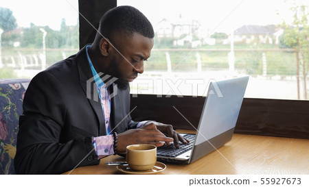 Black businessman is working typing a message on laptop sitting in summer cafe. 55927673
