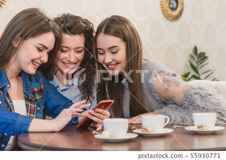 Three friends sitting in a cafe with a smart phone and having a funny conversation. Good girls with Three friends sitting in a cafe with a smart phone and having a funny conversation. Good girls with 55930771