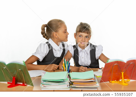 Girls are sitting at a school desk, one whispers 55935107