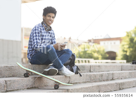 Cheerful teenager using smartphone sitting on stairs against cityscape Cheerful teenager using smartphone sitting on stairs against cityscape 55935614