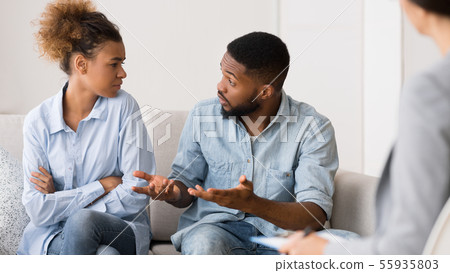 Afro Husband Talking To Wife Sitting At Couples Therapist's Office Afro Husband Talking To Wife Sitting At Couples Therapist's Office 55935803