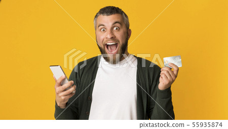 Emotional man holding credit card and smartphone 55935874