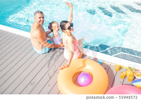 Parents and daughter feeling cheerful resting near pool Parents and daughter feeling cheerful resting near pool 55948572