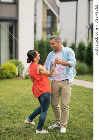 Husband dancing with wife and smiling while feeling happy Husband dancing with wife and smiling while feeling happy 55948862