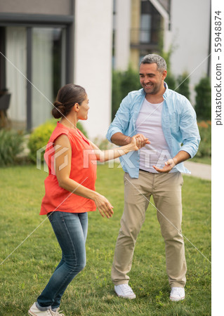 Wife wearing jeans dancing with husband near cottage house Wife wearing jeans dancing with husband near cottage house 55948874