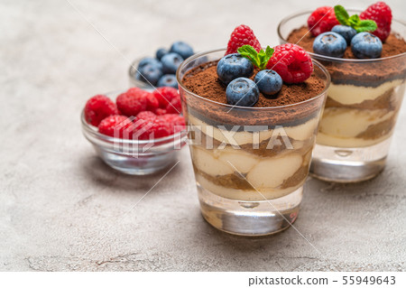 Classic tiramisu dessert with blueberries and raspberries in a glass and bowls with berries on Classic tiramisu dessert with blueberries and raspberries in a glass and bowls with berries on 55949643