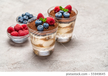 Classic tiramisu dessert with blueberries and raspberries in a glass and bowls with berries on Classic tiramisu dessert with blueberries and raspberries in a glass and bowls with berries on 55949645