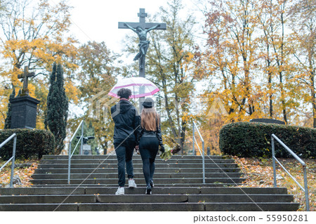 Man and woman walking up steps on cemetery towards a cross 55950281