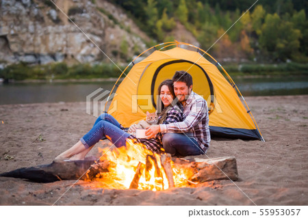 People, tourism and nature concept - Man embrace woman sitting near a fire People, tourism and nature concept - Man embrace woman sitting near a fire 55953057