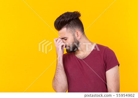Stylish sad pensive young man with a beard in a burgundy t-shirt posing on a yellow background 55954902