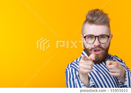Funny young man with a mustache and a beard and glasses shows on you on a yellow background with Funny young man with a mustache and a beard and glasses shows on you on a yellow background with 55955015