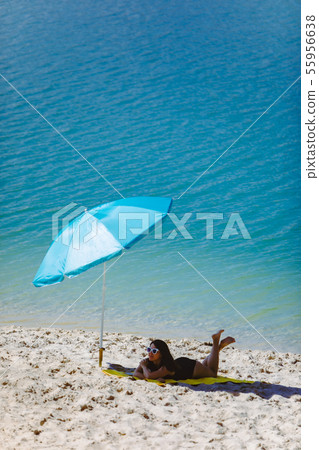woman in swimsuit walking by sand beach blue sun umbrella and yellow blanket 55956638
