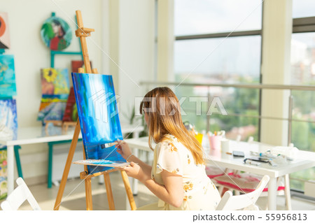 Art class, drawing and creativity concept - Female student sitting in front of easel with palette Art class, drawing and creativity concept - Female student sitting in front of easel with palette 55956813