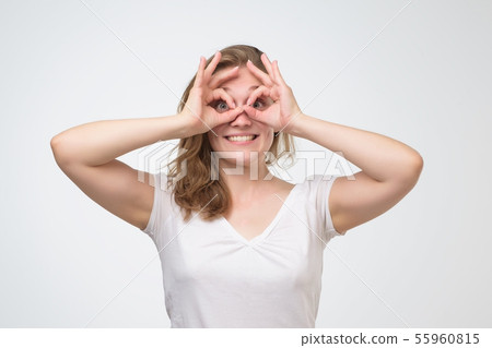 Girl with surprised face holding fingers in ok sign near eyes like glasses. 55960815