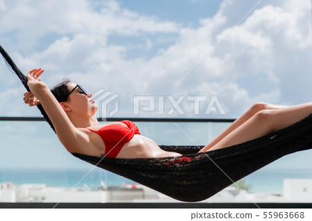 Beautiful girl relaxing in a hammock over a pool on a rooftop of a luxury hotel. View on a blue Beautiful girl relaxing in a hammock over a pool on a rooftop of a luxury hotel. View on a blue 55963668