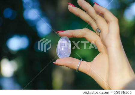 Female hand with transparent amethyst quartz yoni egg for vumfit, imbuilding or meditation. Shining 55976165