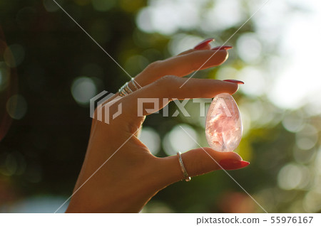Close up photo of female hand with transparent amethyst yoni egg for vumbuilding. Quartz crystal egg 55976167