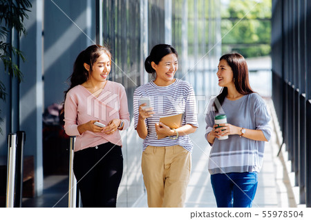 Young Asian business women talking while walking in office building in casual wear Young Asian business women talking while walking in office building in casual wear 55978504