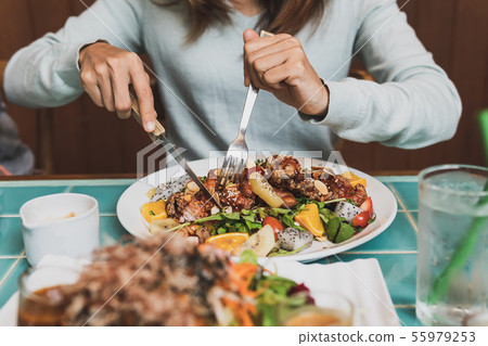 Young woman using knife and fork to cutting meat Young woman using knife and fork to cutting meat 55979253