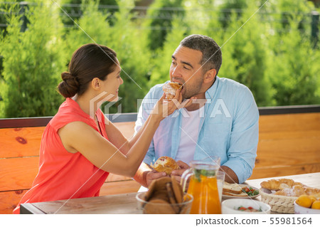 Caring wife smiling while giving some croissant her husband 55981564