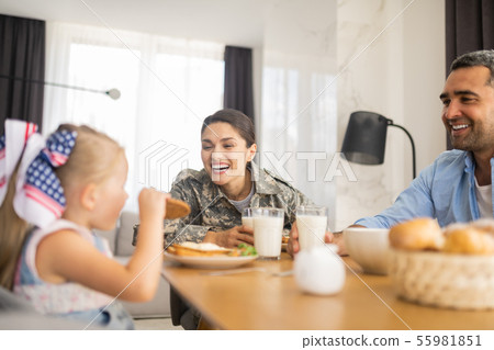 Military woman laughing while looking at her daughter eating cookie Military woman laughing while looking at her daughter eating cookie 55981851