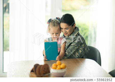 Daughter sitting near mom in military uniform and watching cartoon Daughter sitting near mom in military uniform and watching cartoon 55981952