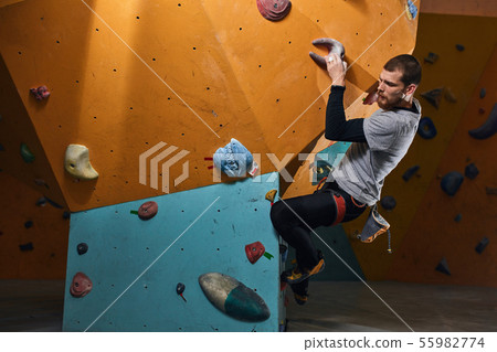 Handsome athletic boulderer training hard at indoor climbing settings 55982774