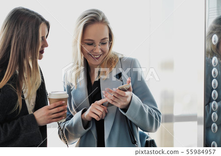 Two beautiful girls, a blonde and a brunette, are wearing a coat in a glass elevator with a window Two beautiful girls, a blonde and a brunette, are wearing a coat in a glass elevator with a window 55984957
