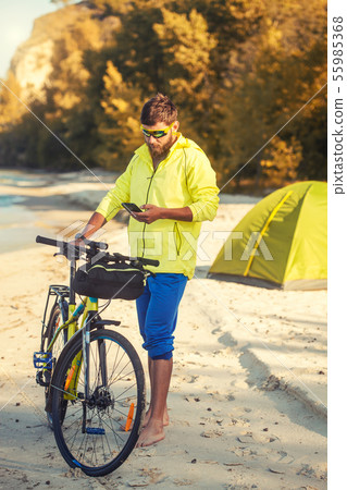 bearded man cyclist rides along the sandy beach on a mountain bike. 55985368