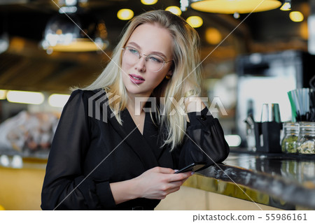 A young beautiful blond woman with glasses sits at the bar in a yellow interior. Drinks alcoholic A young beautiful blond woman with glasses sits at the bar in a yellow interior. Drinks alcoholic 55986161