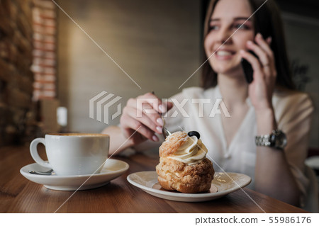 A young beautiful brunette girl in a loft-style cafe sits at a table by the window, drinks coffee 55986176