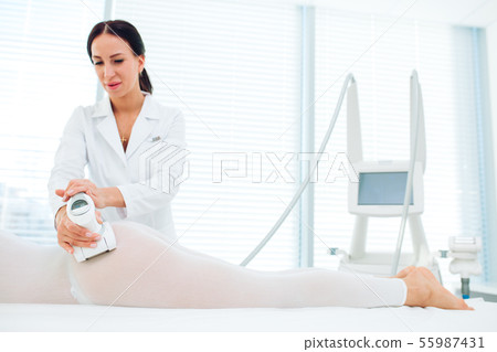 Brunette cosmetological physician performing LPG massage at aethstetic medicine centre. 55987431