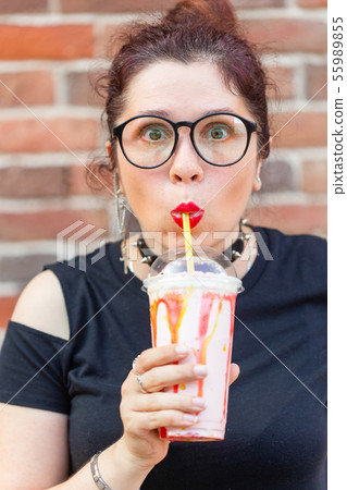 Charming cheerful young stylish girl holding a milkshake with a straw on a brick wall background 55989855