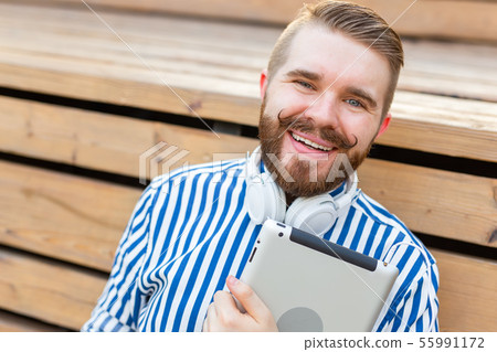 Portrait of a handsome young student guy with a mustache and a beard relaxing in a park with 55991172