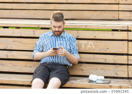 Pensive serious young male hipster student with a mustache and beard writing sms message to his 55991345