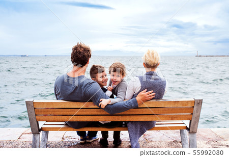 Young family with two small children sitting on bench outdoors on beach. Young family with two small children sitting on bench outdoors on beach. 55992080