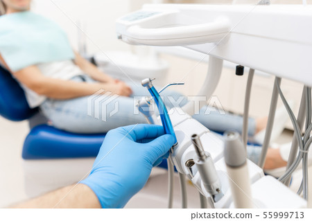 Close-up hand of dentist in the glove holds dental high speed turbine. The patient in blue chair at 55999713