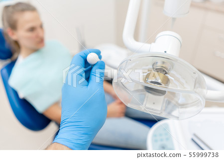 Close-up hand of dentist in the glove adjusts the lamp. The patient in blue chair at the background 55999738