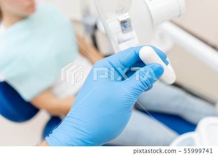 Close-up hand of dentist in the glove adjusts the lamp. The patient in blue chair at the background 55999741