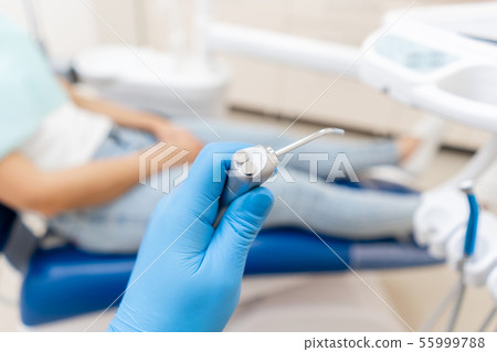 Close-up hand of dentist in the glove holds Gun dental water and air. The patient in blue chair at 55999788