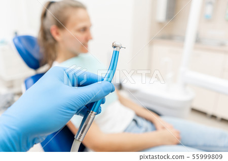 Close-up hand of dentist in the glove holds dental high speed turbine. The patient in blue chair at 55999809