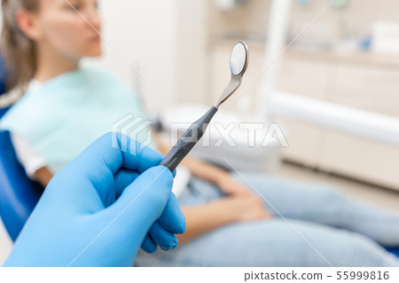 Close-up hand of dentist in the glove holds tool probe and mirror. The patient in the dental chair 55999816