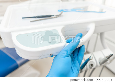 The hand of the dentist in the glove presses the control buttons of the chair.. Dental work in 55999903