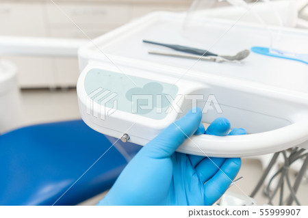 The hand of the dentist in the glove presses the control buttons of the chair.. Dental work in 55999907